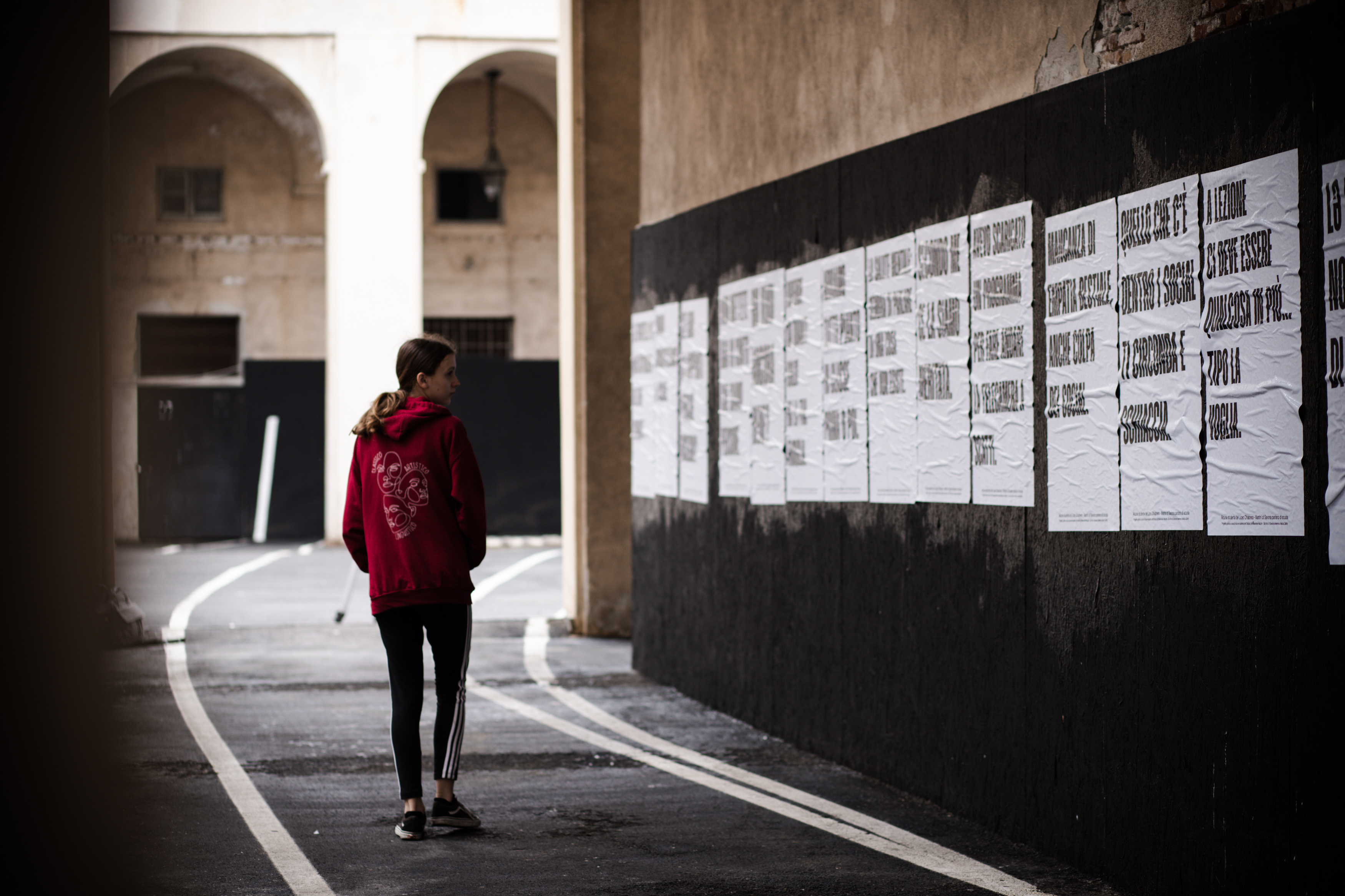 A person standing in a street next to a wall with white posters